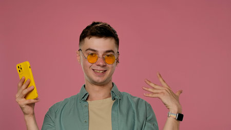 Man Wearing Yellow Sunglasses with Pink Background and Yellow Phoneの写真素材