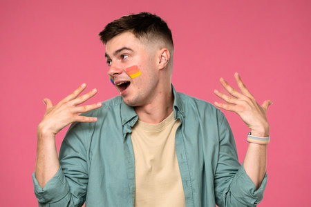 Joyful Young Man with Colorful Face Paint on Pink Backgroundの写真素材