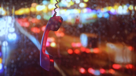 Vintage phone receiver hanging against rainy neon city backgroundの写真素材