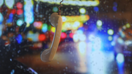 Vintage phone receiver hanging against rainy neon city backgroundの写真素材