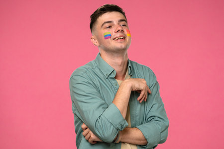 Young person with pride flags painted on face against pink backgroundの写真素材