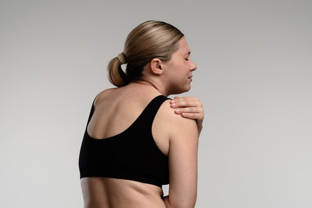 Woman in Black Top Experiencing Shoulder Discomfort Indoorsの写真素材