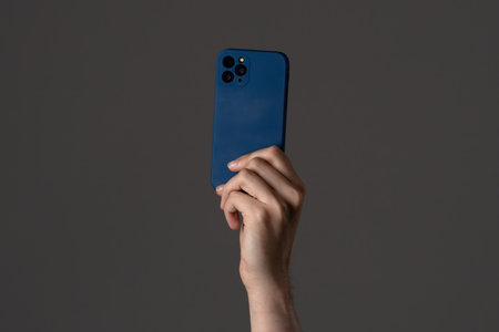 Blue Smartphone Held Up Against Dark Backgroundの写真素材