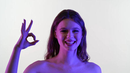 Young Woman Showing Okay Gesture with Colorful Lighting Effectの写真素材
