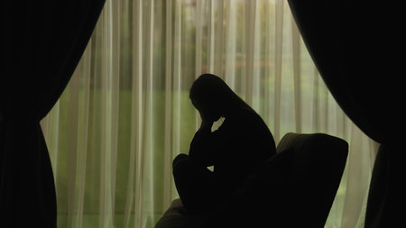 Silhouette of a distressed woman in front of backlit curtainsの写真素材