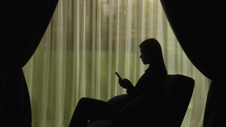 Silhouette of a Woman Using Smartphone by Windowの写真素材