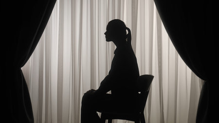 Silhouette of a distressed woman in front of backlit curtainsの写真素材