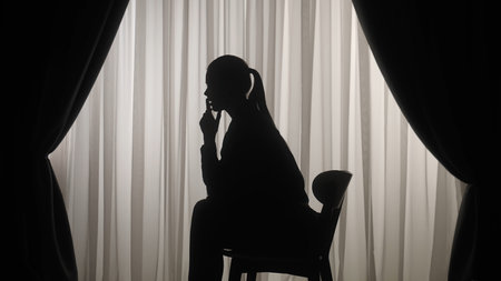 Silhouette of a distressed woman in front of backlit curtainsの写真素材