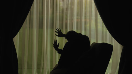 Silhouette of a woman praying in a pensive pose in the light of the windowの写真素材