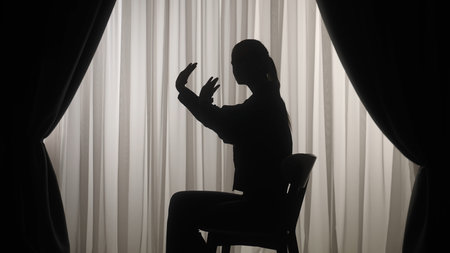 Silhouette of a woman sitting on a chair and showing a stop gesture.の写真素材