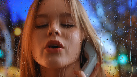 Young Woman Talking on Phone with Rainy Window Backgroundの写真素材