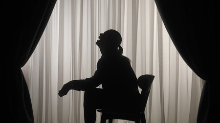Silhouette of a distressed woman in front of backlit curtainsの写真素材