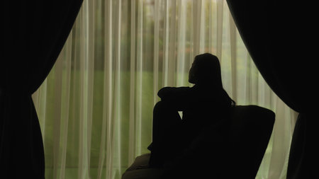 Silhouette of a distressed woman in front of backlit curtainsの写真素材
