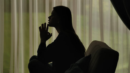 Silhouette of a distressed woman in front of backlit curtainsの写真素材