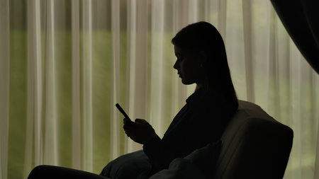 Silhouette of a Woman Using Smartphone by Windowの写真素材