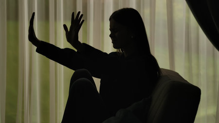 Silhouette of a woman sitting on a couch and showing a stop gesture.の写真素材