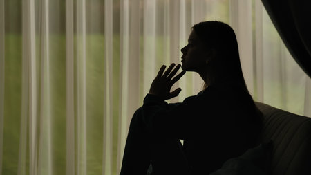 Silhouette of a distressed woman in front of backlit curtainsの写真素材