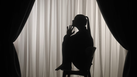Silhouette of a distressed woman in front of backlit curtainsの写真素材