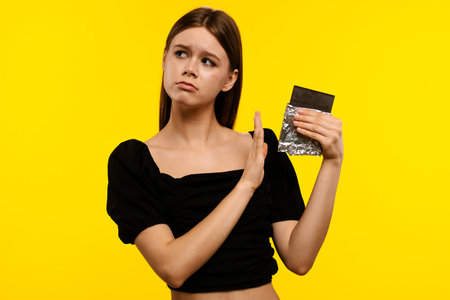 Woman Refusing Chocolate Against Bright Yellow Backgroundの写真素材