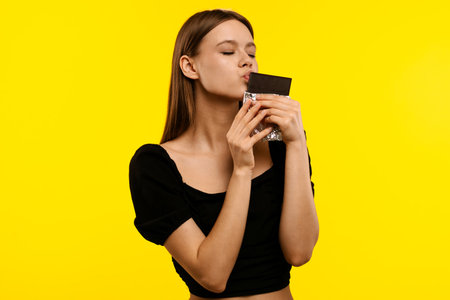 Woman Enjoying Chocolate in Foil on Yellow Backgroundの写真素材