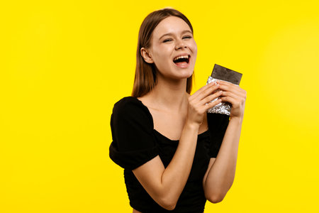 Happy Woman Enjoying Chocolate Against Yellow Backgroundの写真素材