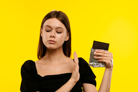 Woman Refusing Chocolate on Bright Yellow Backgroundの写真素材