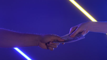 Hands Exchanging Stack of Cash Against Neon Background