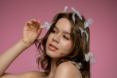 Female model with natural beauty posing with white feathers in her hair on pink backgroundの写真素材