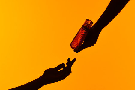 Silhouette of Hands Passing a Perfume Bottle on Orange Background
