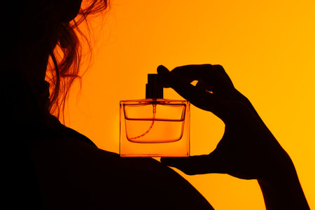 Elegant Silhouette with Woman Holding Perfume Against Orange Background