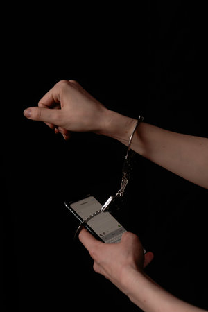 Hands in Handcuffs Using Smartphone Against Black Background