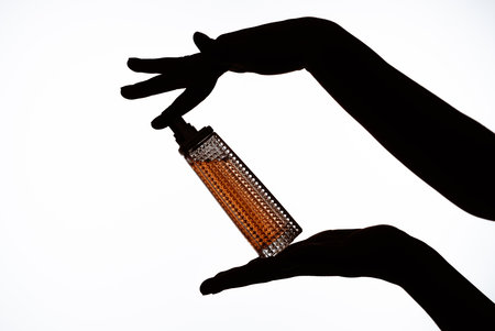 Elegant Glass Bottle with Aromatic Liquid Held in Artistic Silhouetteの写真素材