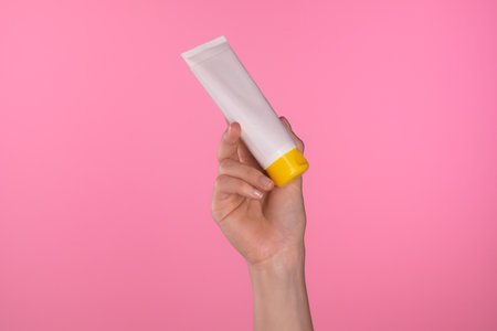 Person Holding White Tube with Yellow Cap Against Pink Backgroundの写真素材