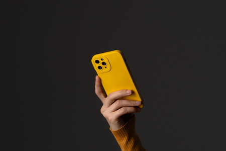 Person Holding Smartphone with Bright Yellow Case in Dark Setting