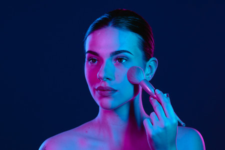 Young Woman with Makeup Brush in Colorful Lighting Setupの写真素材