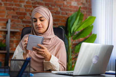 Women in Office Setting with Notebook and Laptopの写真素材
