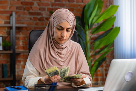 Woman in Hijab Counting Money at Her Office Deskの写真素材