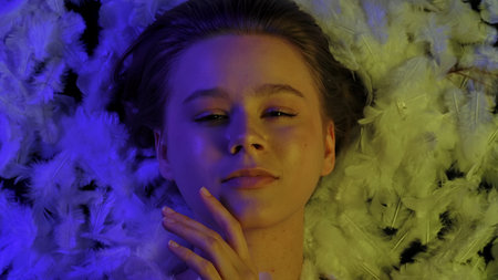 Sensual top view of young woman on feather bed in dramatic colored light