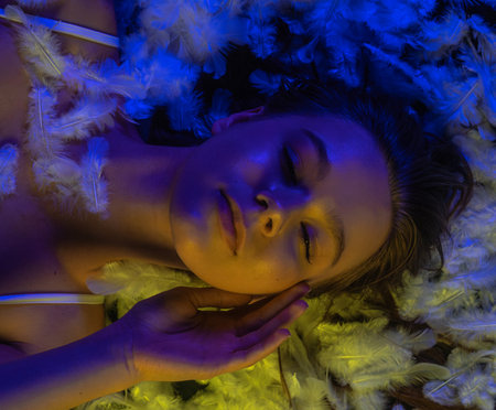 Sensual top view of young woman on feather bed in dramatic colored lightの写真素材