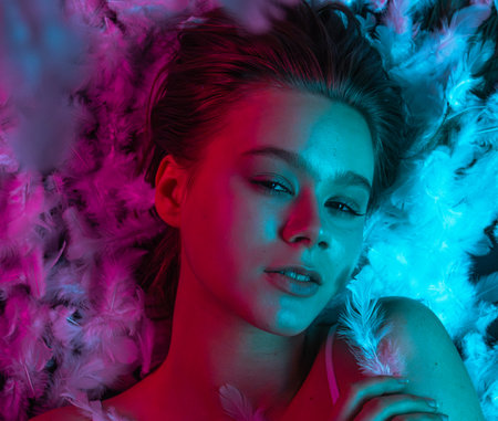 Neon lit beauty top shot with feathers and sensual facial expression