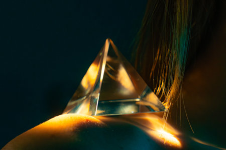 Glass prism reflecting light on woman shoulder in artistic low key setup