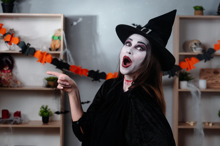 A vampire witch in a black cloak and hat points her finger to the side