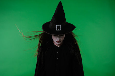 A witch with vampire makeup, in black cloak and hat, stares menacingly at the camera