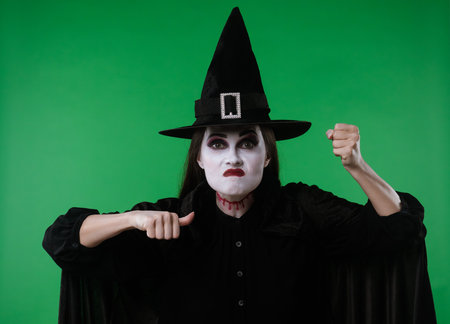 A witch with vampire makeup, wearing a black cloak and hat, looks at the camera and appears very angryの写真素材