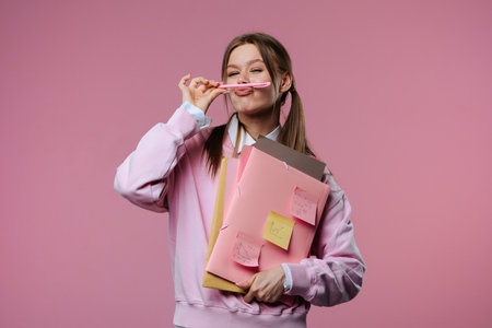 A young female student poses cheerfully, holding folders and notes in her hands