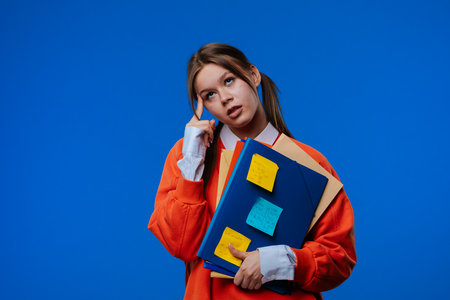 A young female student upset, holding folders and notes in her hands.