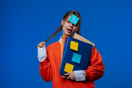 A young female student poses with a sticker on her forehead, holding folders and notes in her handsの写真素材