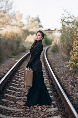 Woman with Vintage Suitcase on Railroad Tracks in Autumnの写真素材