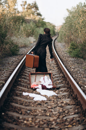 Woman with Vintage Suitcase Walking Along Railroad Tracksの写真素材