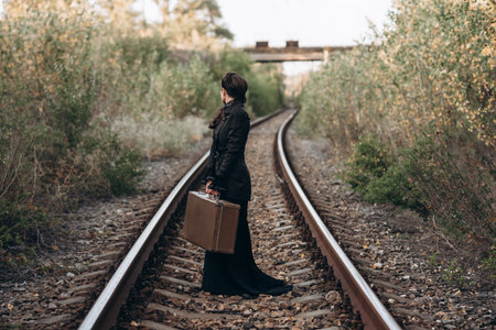 Woman with Vintage Suitcase on Railroad Tracks in Autumnの写真素材